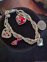 Silver tone bracelet with heart and decorative charms laid on black velvet display, showing front side details.