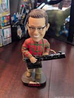 Harold bobblehead figurine on a dark surface showing details of face, clothing, and keyboard object.