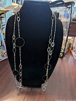 Photo displaying the long silver tone necklace on a black neck display, showing the mix of oval and circular links, featuring larger round loops spaced along the chain.
