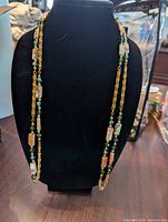 Full-length view of the long necklace displayed on a black stand showing abalone and bead details.