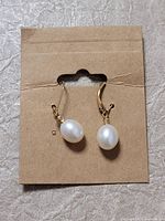 Front view of two new pearl drop earrings on a cardboard holder, showing white oval pearls hanging from small curved gold hooks.