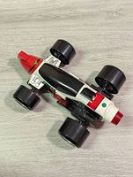 Top-down view of the Robotic Arsenal Mobilizer vehicle showing its aerodynamic shape and black, white, red, and green color scheme with four large black wheels.