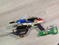 The complete assembled toy blaster showing all parts connected, mainly white with blue black and green components accented with gold.