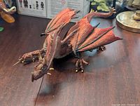 Full body view of reddish-brown dragon figure with wings spread resting on wooden surface