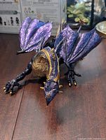 Photo showing front view of dragon figure with purple wings and gold belly with detailing of claws and head.