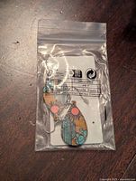 Clear photo of earrings in sealed plastic bag showing teardrop cork earrings with colorful cactus and sun design.