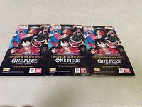 Three unopened booster packs of One Piece Card Game laid flat on a surface.