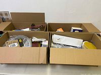 Four large cardboard boxes filled with various miscellaneous new and used items including hardware, cables, and tools.