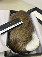 Photo of the Belle Tress Peppermint Hue hairpiece lying in open box showing hair color and texture with label attached.
