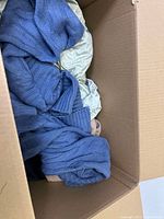 Box showing blue knitted sweater and other clothes inside cardboard box