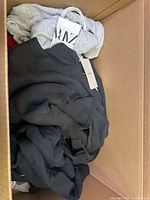 Box of assorted knitwear in black and grey with Zara tag visible.
