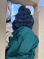Box opened showing assorted clothes piled inside, black, green, white/cream pieces visible