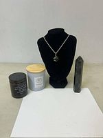 Full lot setup showing black and white candles, silver necklace with stone pendant on black stand, and crystal obelisk
