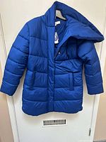 Blue vegan down coat hanging on hanger, showing front with shawl collar, hood, and two patch pockets.