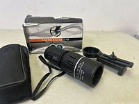 Photo showing the compact monocular telescope, carrying case, mounting bracket, and damaged packaging box on a white surface.
