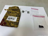 Pair of garnet temple earrings displayed with a patterned cloth pouch and two small resealable plastic bags on a white surface.