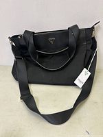 Front view of black Guess carry on bag with logo and attached tag