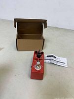 Red Holy War Pedal guitar effects pedal with two black knobs and one footswitch button next to an open cardboard box and a manual