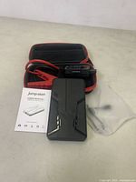 Main jump start booster device laid on surface with user manual and carrying case
