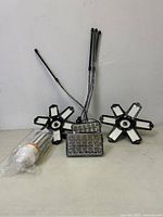 Two star-shaped LED work lights with five adjustable panels each and cooling fans at the center, along with a rolled-up LED strip and a rectangular LED light on table surface against a wall.