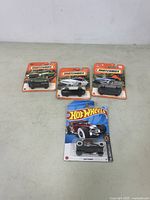 Four new collectible die-cast cars in original packaging: three Matchbox and one Hot Wheels car visible on a plain surface.