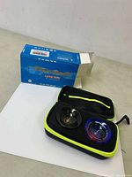 Two metal yoyos, one black and one blue-purple transparent, displayed inside a neon yellow trimmed black zippered carrying case, with the opened blue box behind