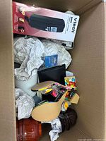 Box displaying VTech cordless phone box, beige high-heeled slipper, small items and packing paper.