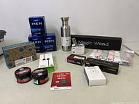 Wide view showing entire lot including boxed men’s cream, insulated bottle, Magic Wand, baby socks, pomade, cables, memory card, and adapter.