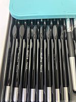 Top view of Nicpro round paint brushes with black handles and silver tips, showing size labels including 3/0, 1, and 4, inside a plastic tray.