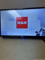 Front view of TV powered on with RCA logo and dog images on screen.