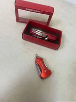 Front view of the Switzerland branded red multi-tool picnic tool in its box, showing the fork and other tools folded inside.