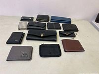 Top view of 13 assorted wallets of various brands and styles laid out on a white surface.