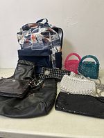 Photo showing a group of assorted purses, backpacks, and clutches arranged against a wall.