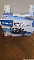 Front view of sealed Swann Advanced Security System box showing brand, series, and number of cameras.