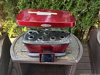 Front view of red Aerogarden hydroponic grower with digital control screen and 7 growing holes visible, placed on outdoor table.