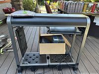 Front view of black metal/plastic hydroponic grower frame with seed pod holes and some accessories in a box under the trays.