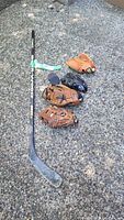 Full lot showing four baseball gloves, hockey stick, and two pucks placed on gravel surface