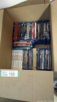 Box containing an assortment of Blu-Ray DVDs arranged in rows including movies and series sets.