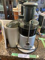 Silver and black Breville Juice Fountain juicer on kitchen counter with recipe book behind it. Shows wear and power cord coiled at base.