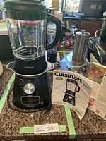 Front view of Cuisinart blend and cook soup and beverage maker on kitchen counter with instruction booklet shown.