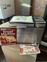 Photo of the stainless steel bread maker with instruction booklet on top plus two bread recipe books in front