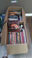 Top view of box filled with various cookbooks packed neatly, showing diversity in cooking themes.