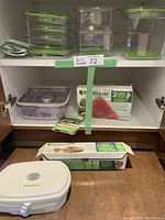 Photo of clear rectangular FoodSaver vacuum sealer containers with green lids stacked in shelving unit along with boxed heat-seal rolls and additional bags.