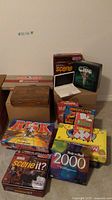 Board games stacked showing Monopoly, Scene It, Clue, Yahtzee and Risk games along with Big Sudoku puzzle book.