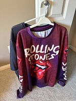 Two Rolling Stones concert shirts on hangers, long sleeve and short sleeve visible, showing front side of long sleeve shirt