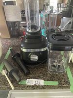 Full view of KitchenAid blender base with tall blending container attached, two muddlers, and additional smaller container with blade assembly on the side, cleaning brush visible.