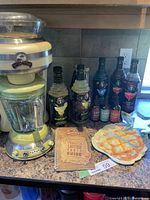 Photo showing the full party pack on a kitchen countertop including the yellow Margaritaville blender, six mixer bottles, recipe book, and margarita platter