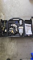 Mastercraft air-powered gravity-feed spray gun and accessories organized neatly in black carrying case on a gray concrete floor.