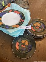 Stack of Noritake dinner and side plates showing colorful fruit and leaf pattern with gold trim.
