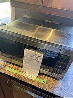 Panasonic microwave oven on kitchen counter with operating manual in front. Exterior shows dust and dirt spots.